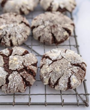 close up top view of a cooling rack cracked cookies that are nearly white on top but the cracks reveals dark chocolaty lines