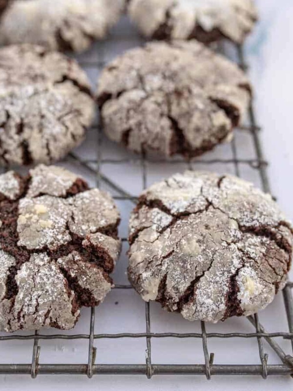 close up top view of a cooling rack cracked cookies that are nearly white on top but the cracks reveals dark chocolaty lines