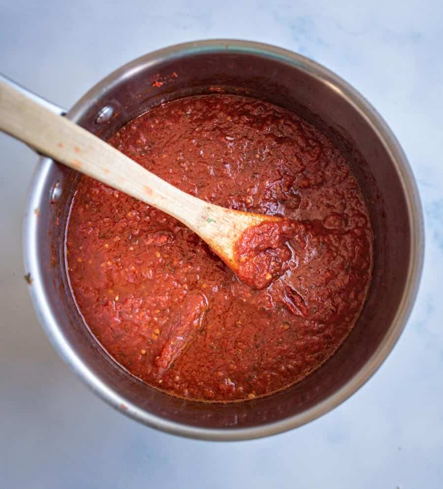top view pot with red pizza sauce and wooden spoon.