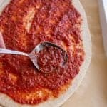 rustic pizza dough with red sauce being smeared with a spoon