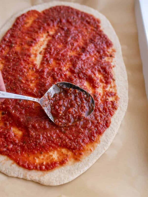 rustic pizza dough with red sauce being smeared with a spoon