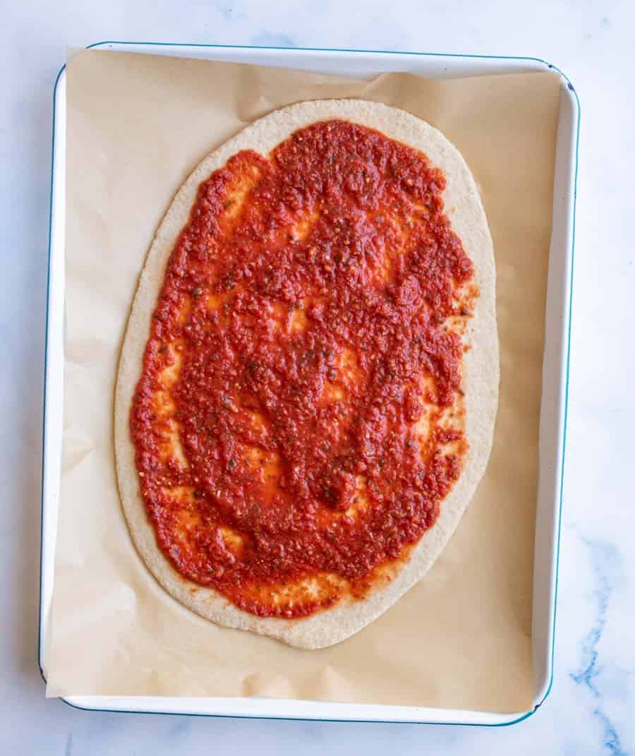 oval rustic pizza dough smeared with red sauce.