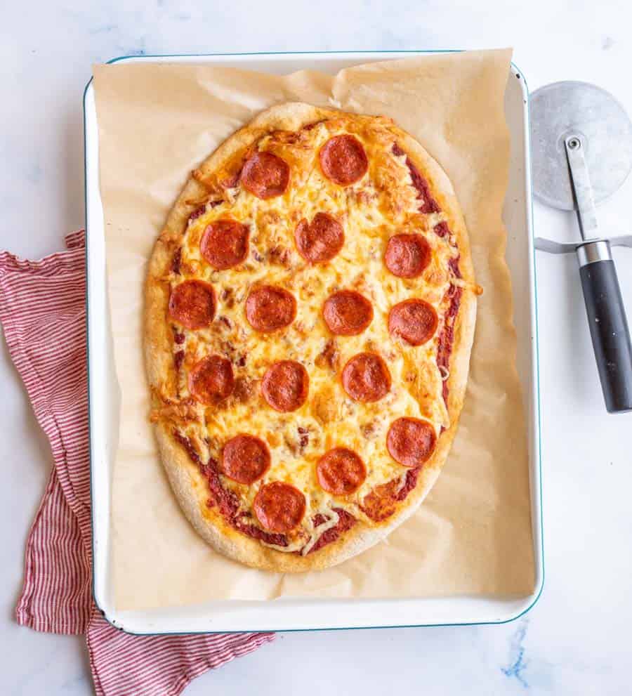 top view - sheet pan with a rustic home made oval shaped cooked pepperoni pizza
