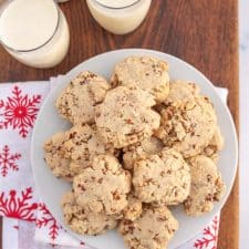 top view - christmas setting on wooden block with egg nog and traditional tan looking pecan sandies cookies on a white plate