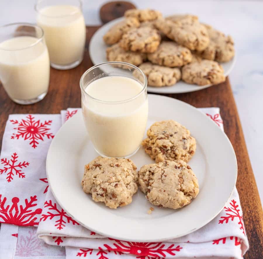 A side view of three pecan sandies on a plate with a milk glass on a white and red snowflake napkin.