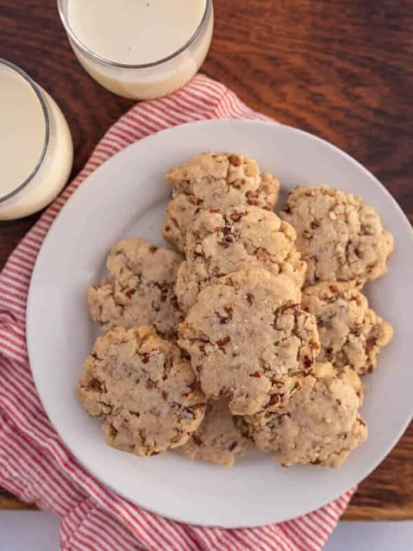 top view -christmas setting on wooden block with egg nog and traditional tan looking pecan sandies cookies on a white plate