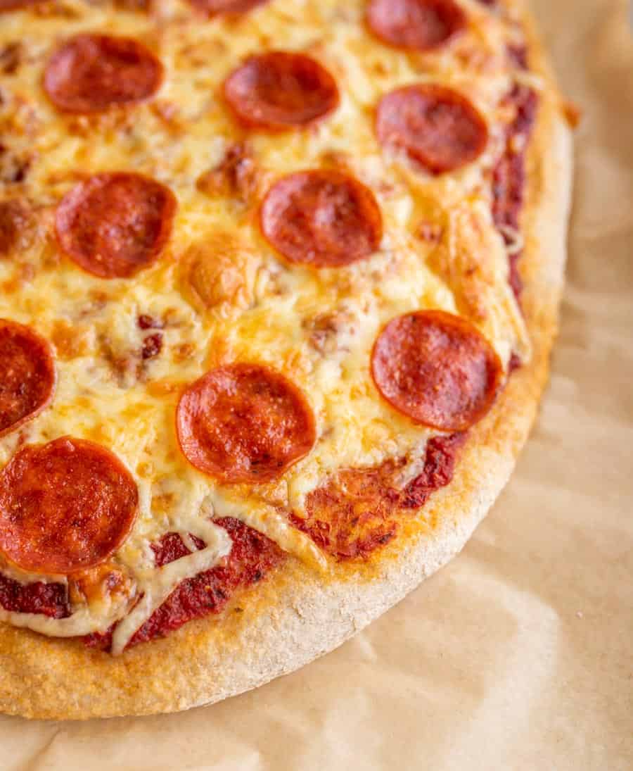 Up close shot of a pepperoni and cheese pizza with whole wheat crust on parchment paper.
