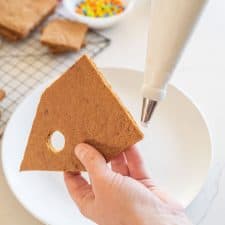 POV a hand putting icing along the bottom of a gingerbread bird house