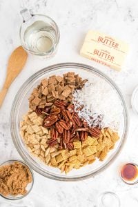 a clear glass bowl of Chex-Mix and pecans and coconut shards.