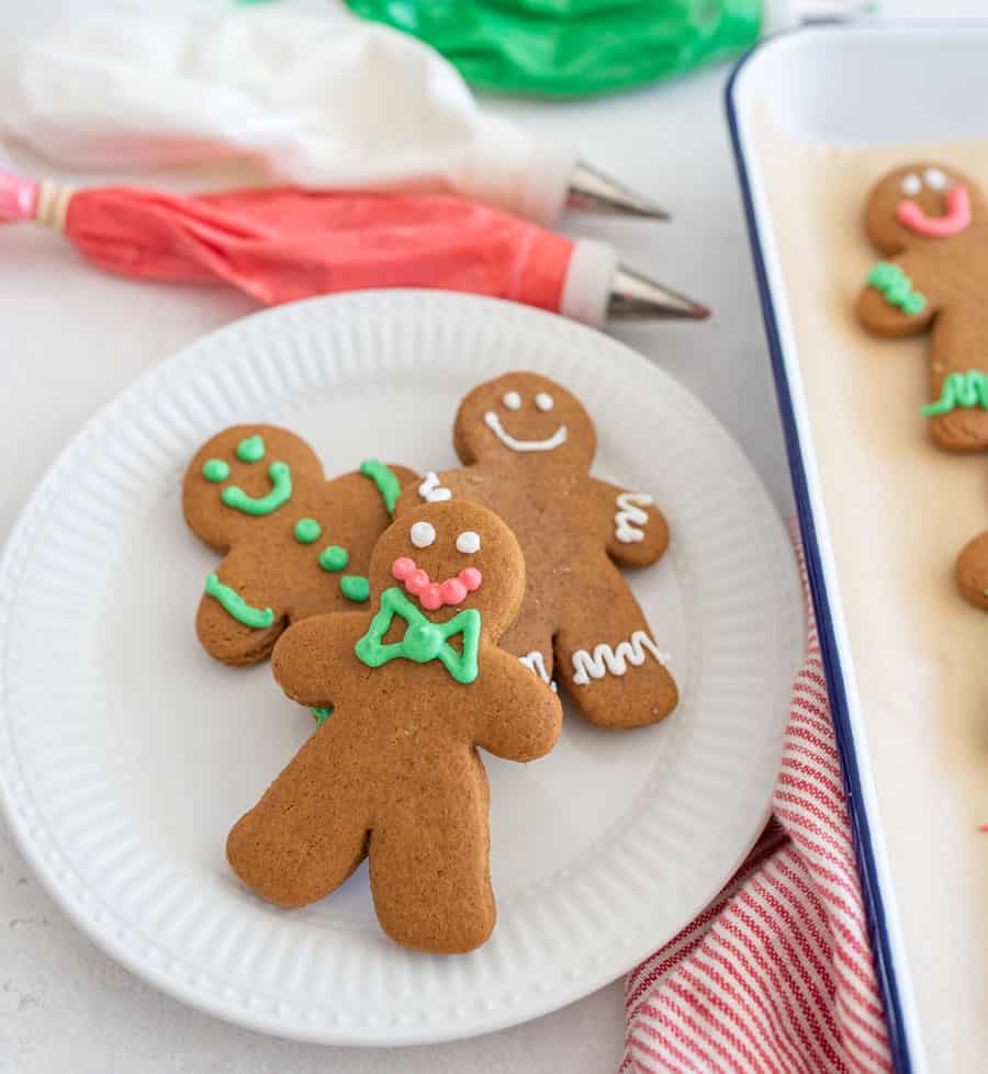 A white plate with decorated vegan gingerbread cookies on it next to decorating icing.