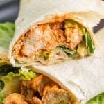 close up very detailed end view of the buffalo chicken wraps - flour tortilla wrapped saucy cooked chicken and lettuce sliced to see what's inside