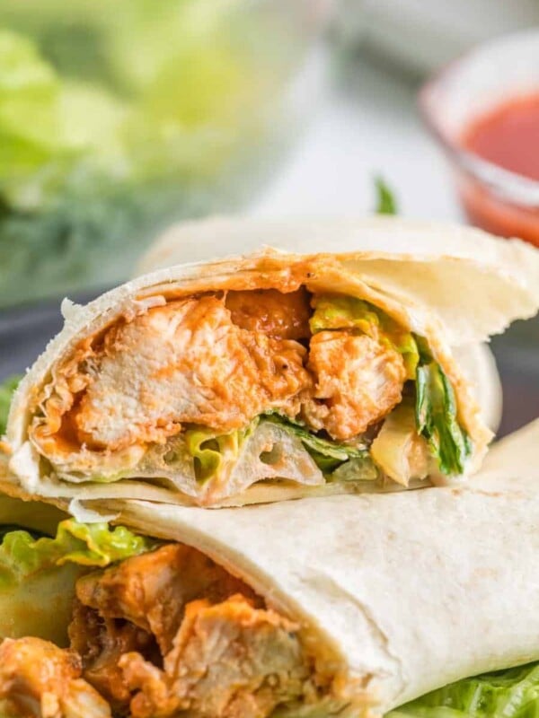 close up, end view buffalo chicken wraps - flour tortilla wrapped saucy cooked chicken and lettuce sliced to see what's inside