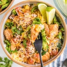 very close view of chicken burrito bowl to see detail of limes and cilantro and cheese avocados and tomatoes with fork