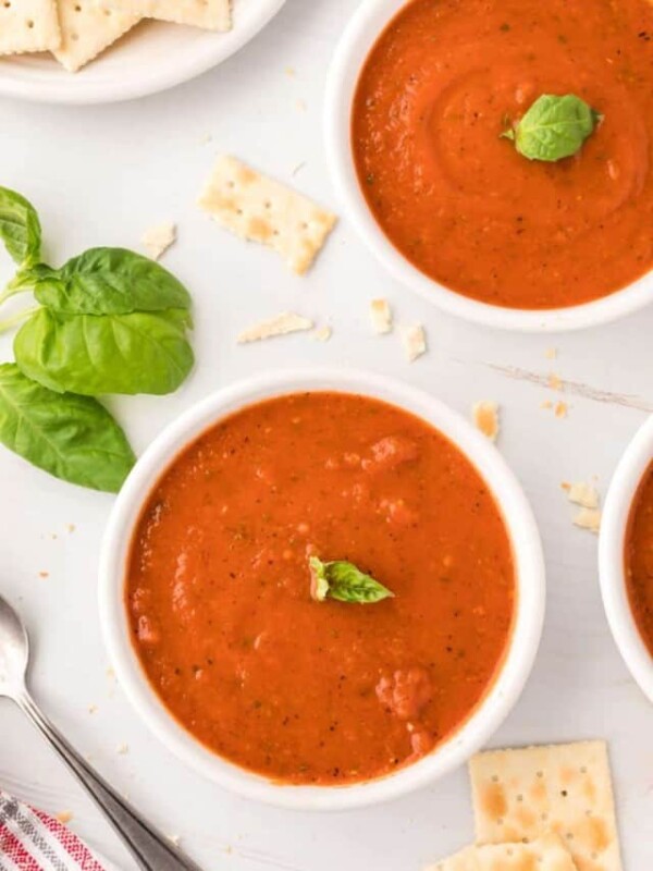 bowls of tomato soup topped with basil and surrounded by crackers