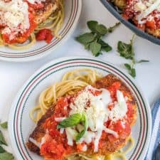 top view chicken parmesan dinner plate - spaghetti pasta and breaded chicken breast with red sauce on top on a white and Italian themed plate