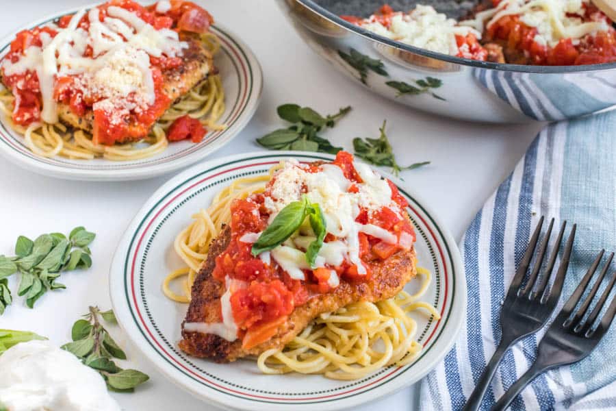 side view chicken parmesan dinner plate - spaghetti pasta and breaded chicken breast with red sauce on top on a white and Italian themed plate