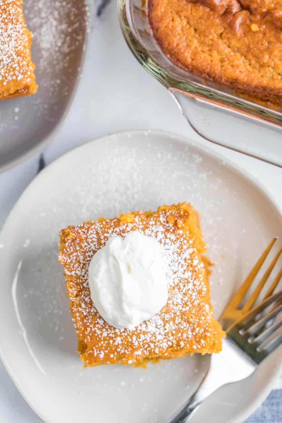 top view close up - square serving of extra thick pumpkin cake on a white plate with a dollop of cream