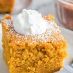 Close up - side view square servings of extra thick pumpkin cake on a white plate with a dollop of cream