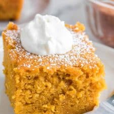 Close up - side view square servings of extra thick pumpkin cake on a white plate with a dollop of cream