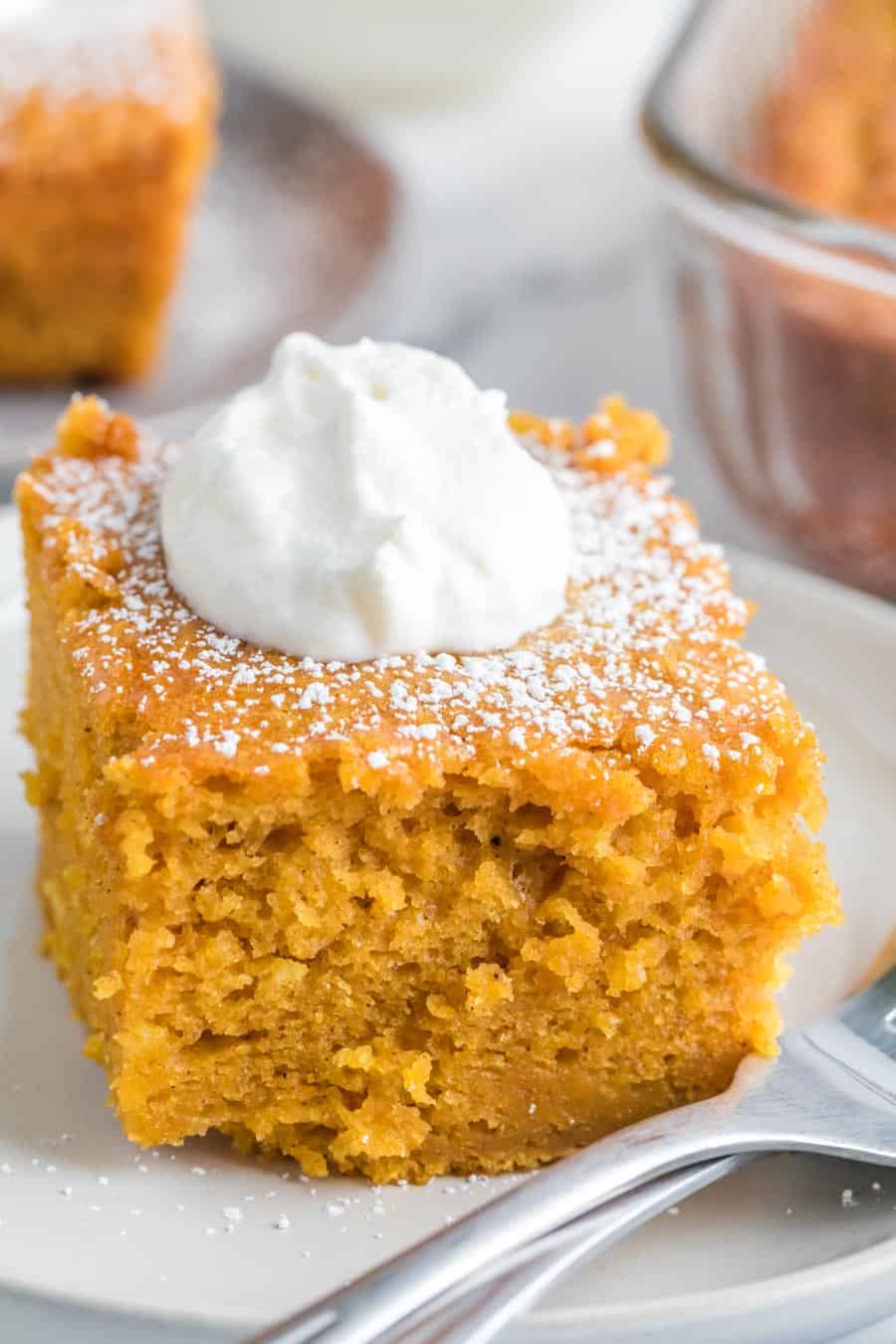 Close up - side view square servings of extra thick pumpkin cake on a white plate with a dollop of cream