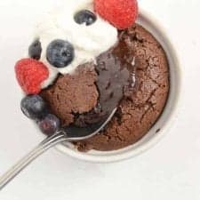 spoon dipping into the soft center of a lava cake with whipped cream and raspberries and blueberries on top