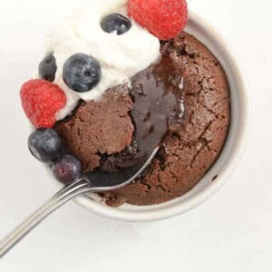 spoon dipping into the soft center of a lava cake with whipped cream and raspberries and blueberries on top