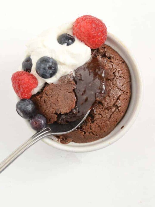 spoon dipping into the soft center of a lava cake with whipped cream and raspberries and blueberries on top