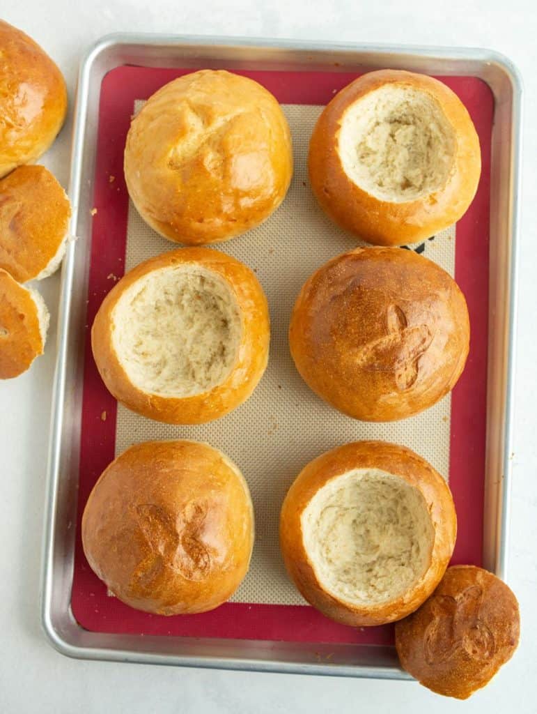 6 large round rolls baked golden brown and a little x on the tops line a silicone baking sheet and a few of the rolls are hollowed for the bread bowl