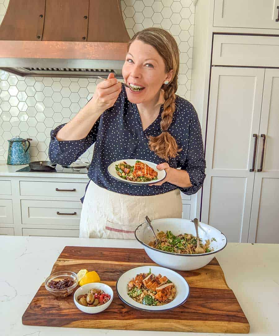 Melissa in her kitchen taking a bite off the completed dish and all of the completed components on the wood block in front of her