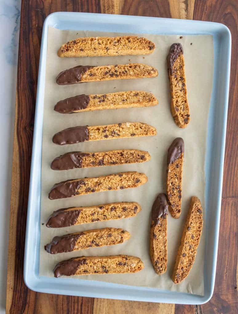 top view of a sheet pan of biscotti on a parchment with chocolate chips and one end lightly covered in chocolate