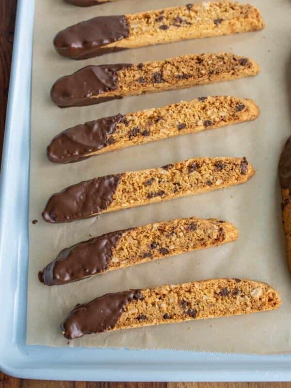 close up of biscotti on a parchment with chocolate chips and one end lightly covered in chocolate on a baking sheet pan
