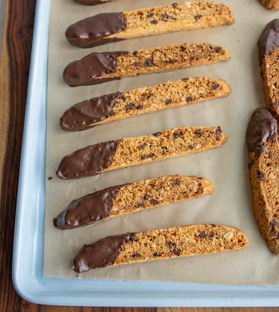 close up of biscotti on a parchment with chocolate chips and one end lightly covered in chocolate on a baking sheet pan
