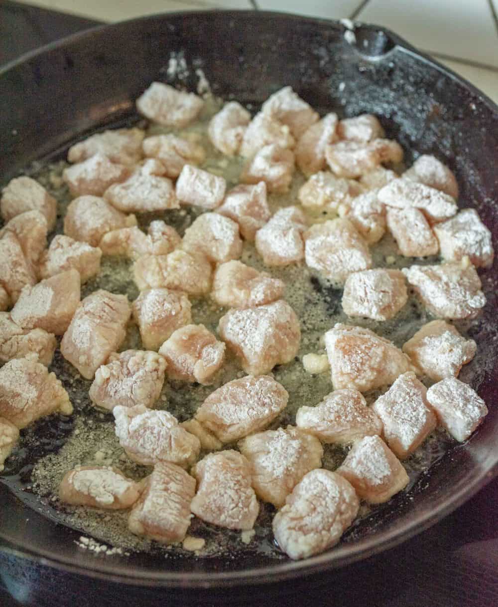 Chopped chicken cooking in a cast iron frying pan.