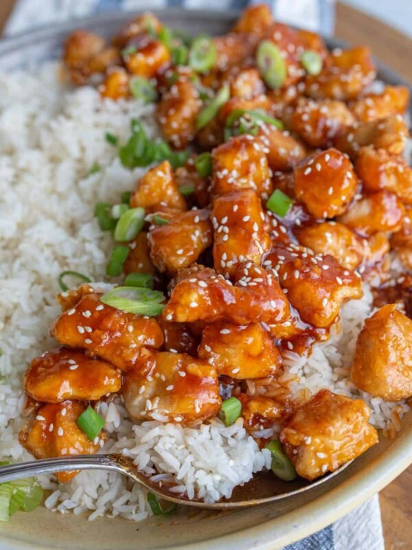a bowl of rice with sticky sesame chicken with chives and green onion on top