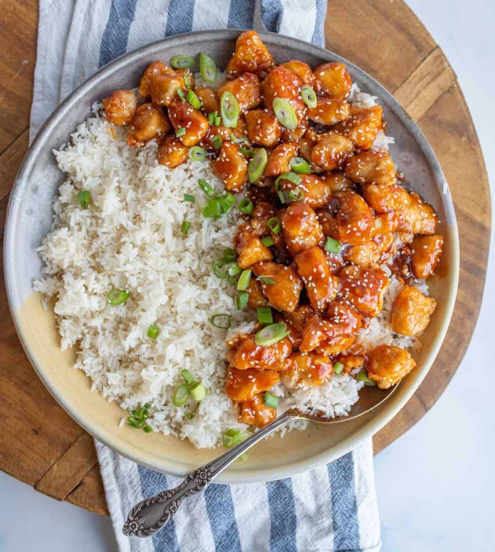 Sesame chicken served over a plate of rice.
