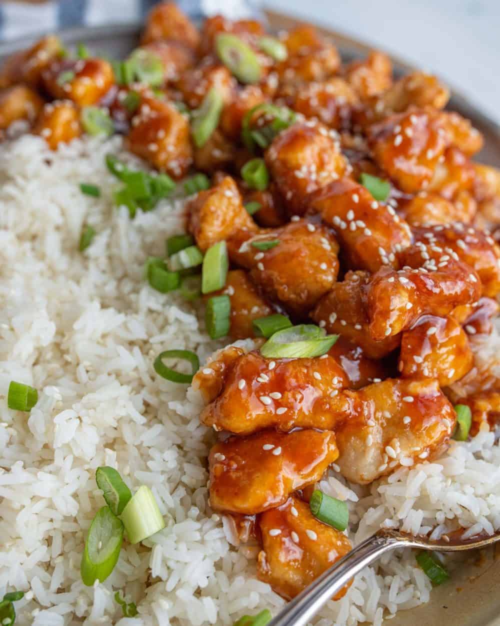 a bowl of rice with sticky sesame chicken with chives and green onion on top.