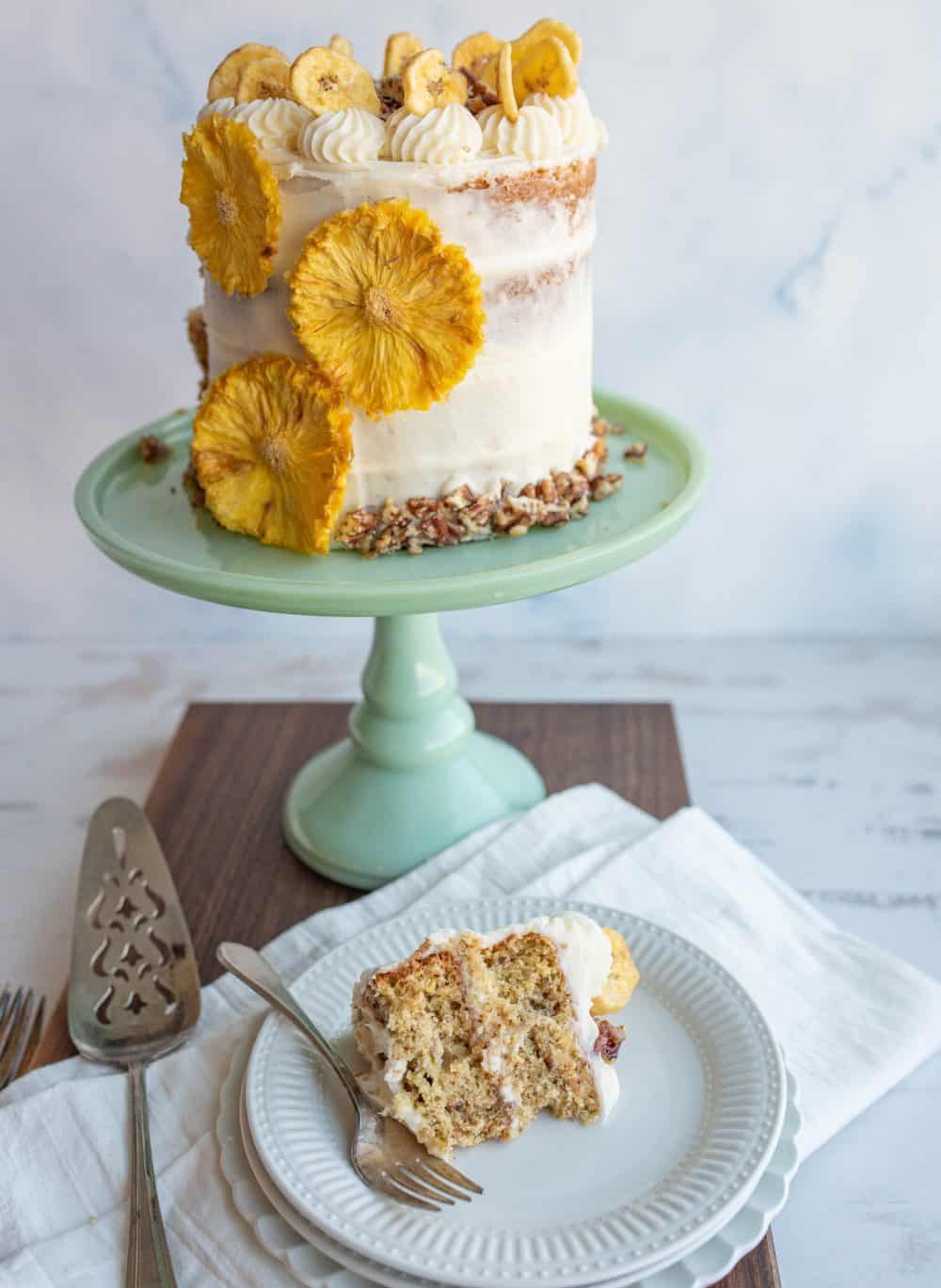 complete hummingbird cake on a teal stand and a slice taken out in front of it.