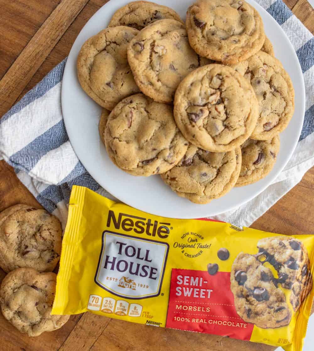 a plate stacked with chocolate chip cookies next to a bag of semi sweet chocolate morsels