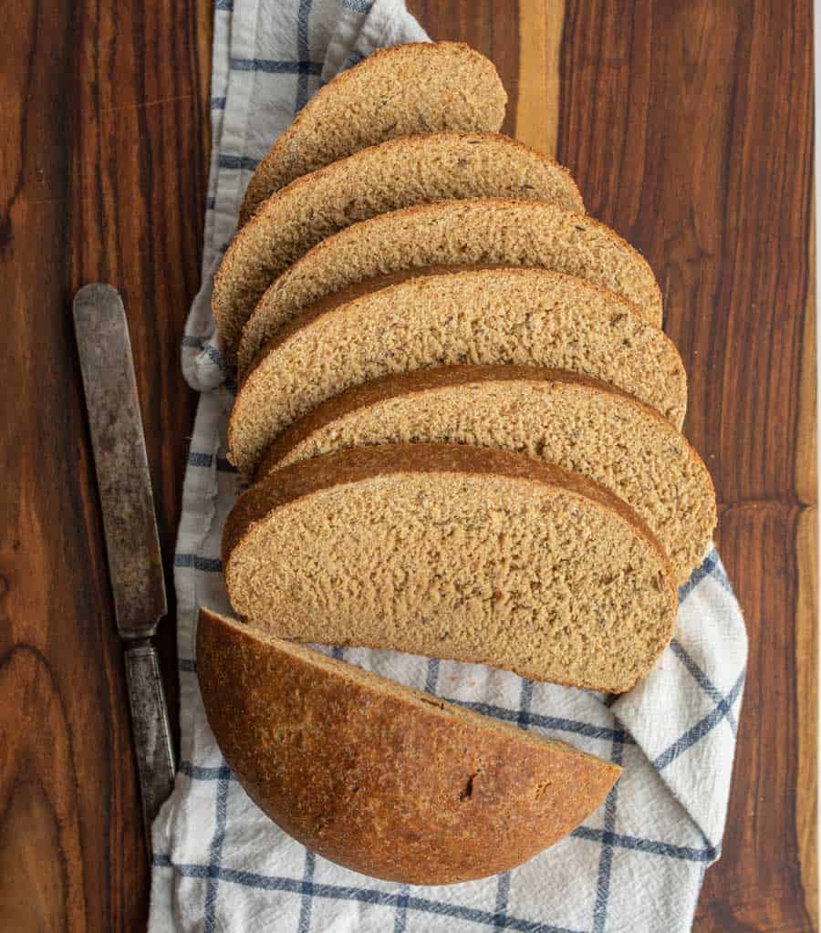 beautiful perfectly round baked rye bread loaf cut into slices on a plaid dish towel.