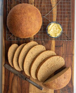 beautiful perfectly round baked bread loaf from a rye bread recipe and then some slices that are buttered.