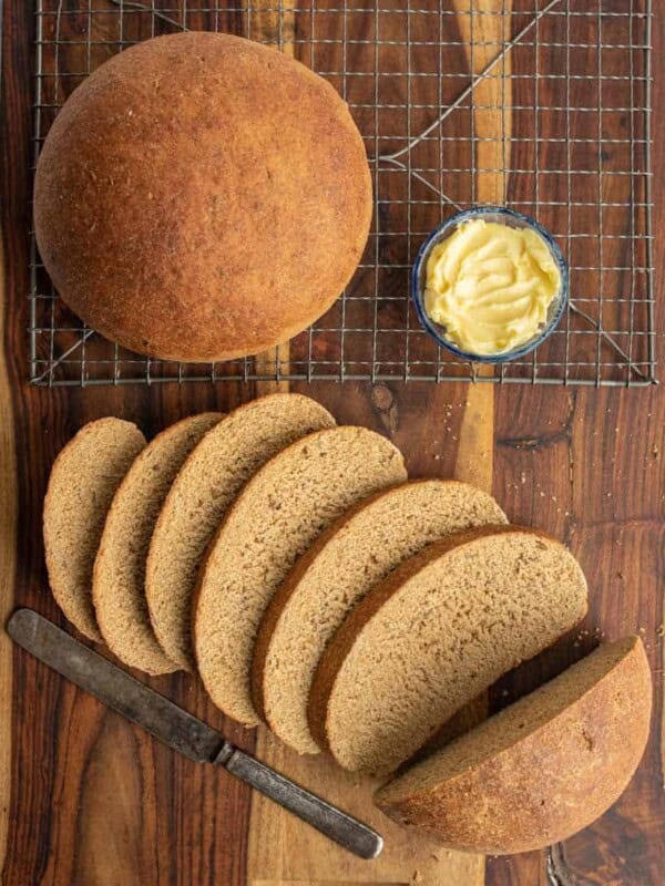 beautiful perfectly round baked bread loaf from a rye bread recipe and then some slices that are buttered.