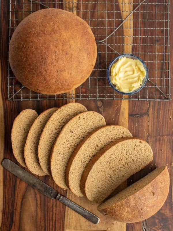 beautiful perfectly round baked bread loaf and then some slices that are buttered