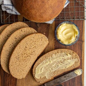 beautiful perfectly round baked bread loaf and then some slices that are buttered