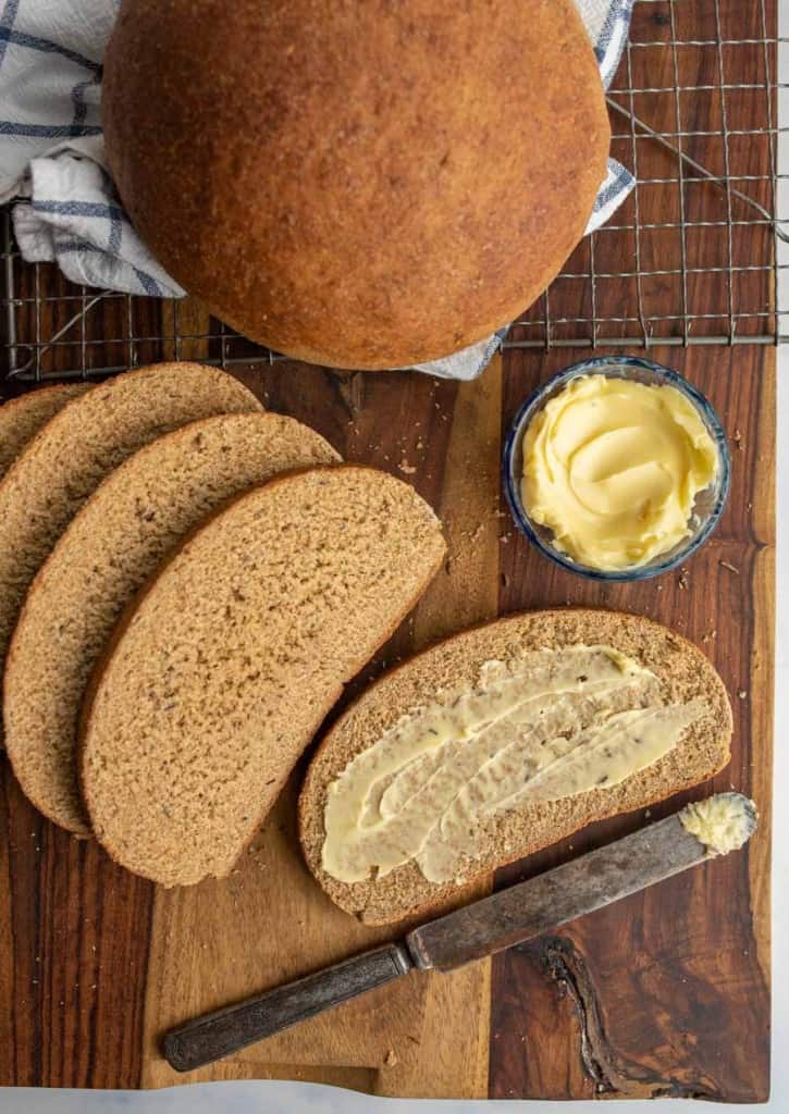 beautiful perfectly round baked bread loaf and then some slices that are buttered