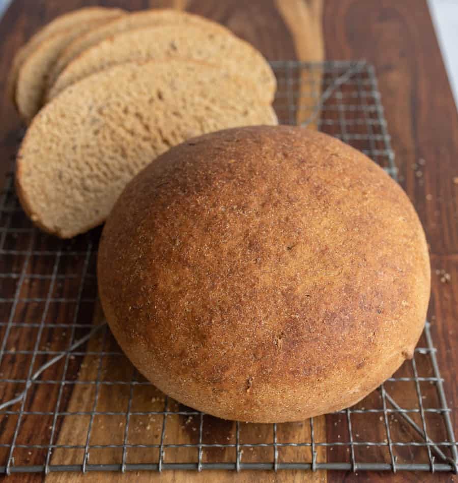 beautiful perfectly round baked rye bread loaf on a cooling rack.