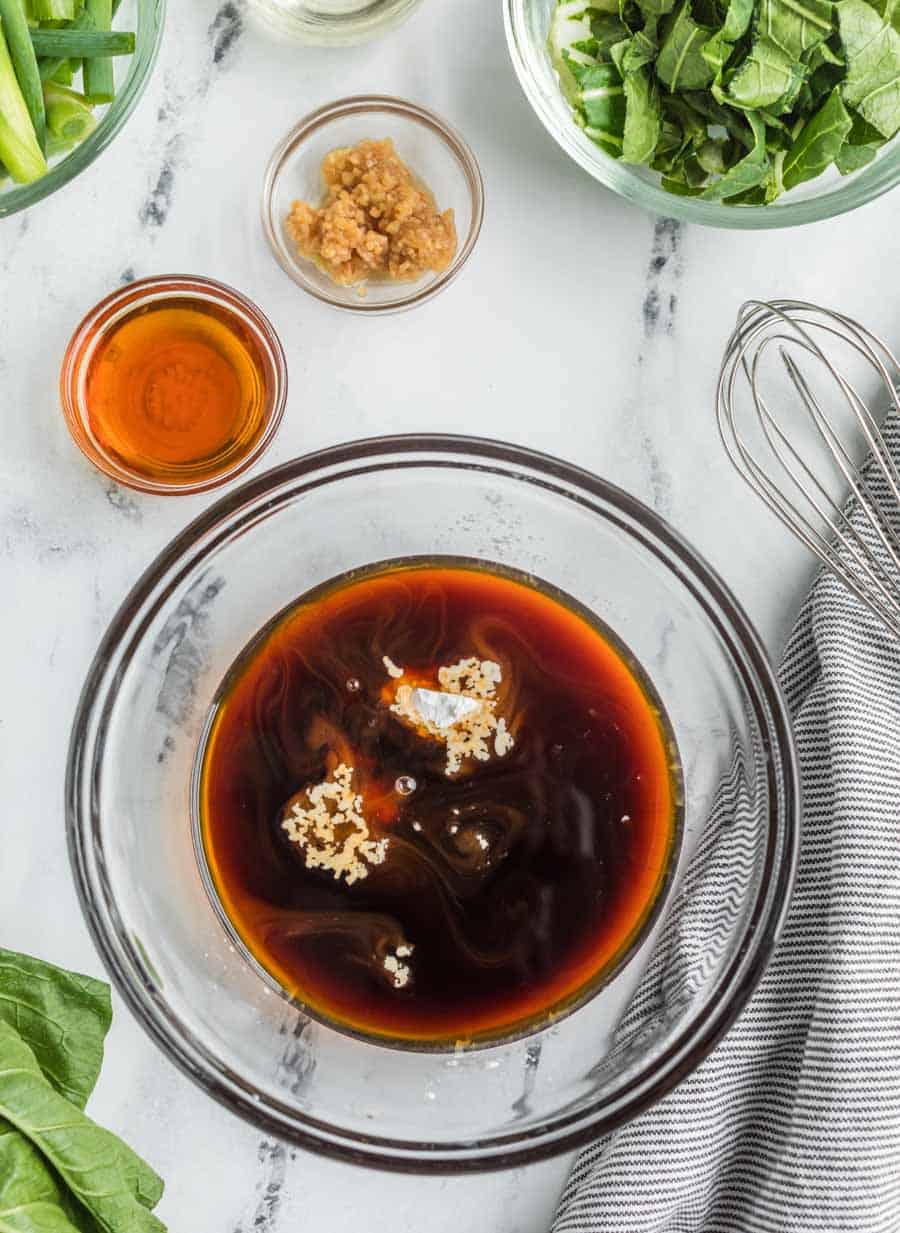 lo mein sauce in a clear bowl and a whisk and more spices to the side.