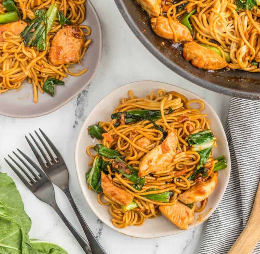 lo mein noodles with cooked boo choy and chicken on a few plates and with the pan