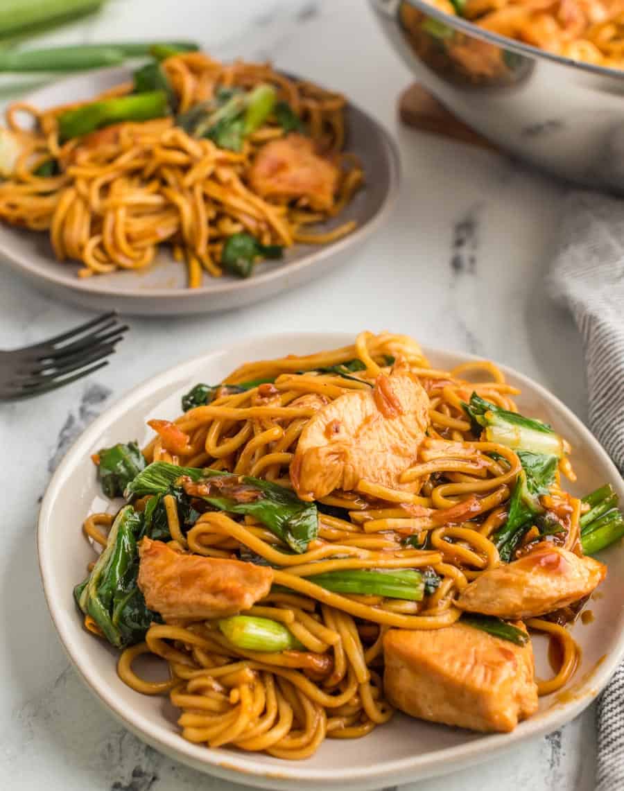 lo mein noodles with cooked boo choy and chicken on a few plates and with the pan.