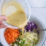 coleslaw ingredients in wedge sections in a white bowl with a POV of a hand pouring in the coleslaw dressing on the top