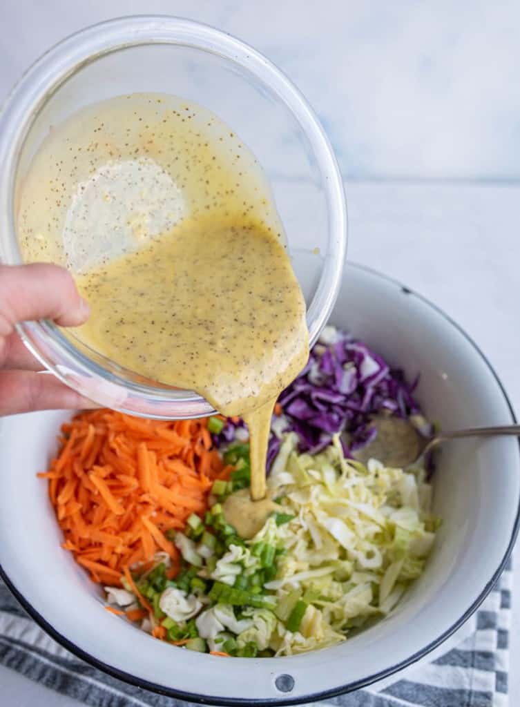 coleslaw ingredients in wedge sections in a white bowl with a POV of a hand pouring in the coleslaw dressing on the top